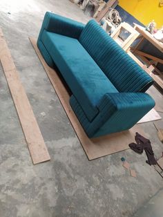 a blue couch sitting on top of a wooden floor next to a piece of plywood