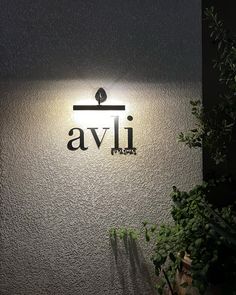 an illuminated sign on the side of a building with plants growing in front of it