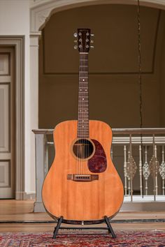 an acoustic guitar sitting on top of a rug in front of a doorway and railing