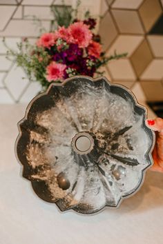 a person holding up a metal object with flowers in the background on a table top