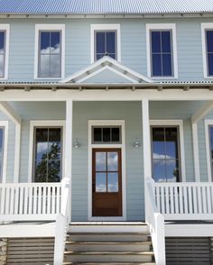 a blue house with white railings and steps leading up to the front door on a sunny day