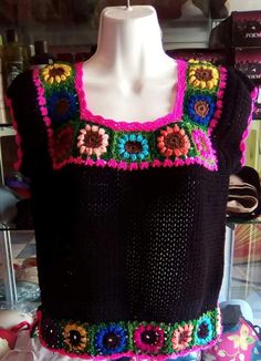 a black sweater with colorful crocheted flowers on the front and sides, sitting on a mannequin