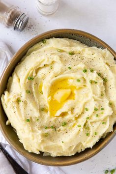 a bowl filled with mashed potatoes on top of a white table cloth next to utensils