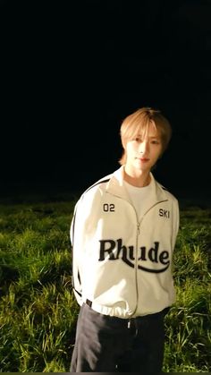 a young man standing in the grass wearing a white jacket with black letters on it