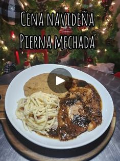 a white plate topped with meat and pasta on top of a wooden table next to a christmas tree