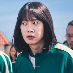 a young man with long hair standing in front of other people wearing green and white jackets