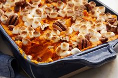 a blue casserole dish filled with sweet potatoes and pecans, topped with marshmallows