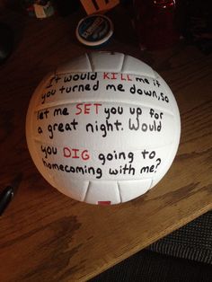 a white volleyball with writing on it sitting on a wooden table next to a pen