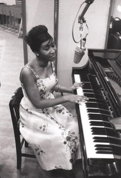 a woman sitting at a piano with a microphone in front of her and she is smiling