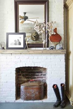 a fire place in a living room with a mirror above it and boots on the floor