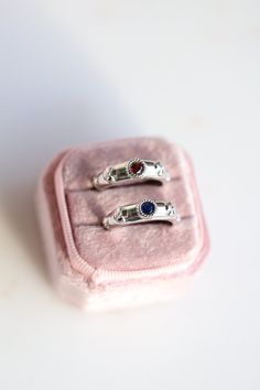 two silver rings sitting on top of a pink velvet case with white and blue stones