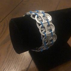 a silver bracelet with blue cords on top of a black velvet ring stand in front of a wooden table