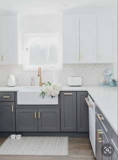 a kitchen with white and gray cabinets, gold pulls on the cabinet doors in front of the sink