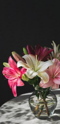 a glass vase filled with pink and white flowers on top of a round tablecloth