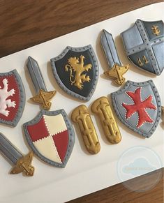 decorated cookies in the shape of shields and swords are displayed on a white board with wood grain