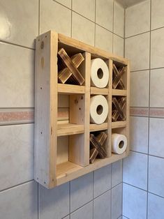 a wooden box with rolls of toilet paper in it on the wall next to a tiled wall