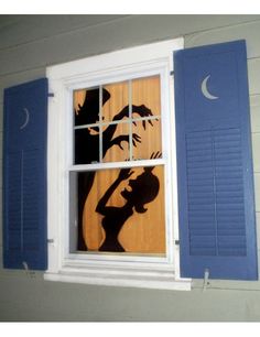 a window with blue shutters and a shadow of a woman holding a bird on it