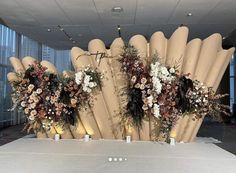 an arrangement of flowers and greenery on top of a table in front of large windows