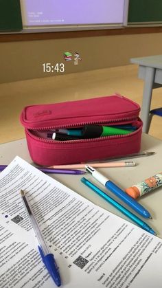 a pink pencil case sitting on top of a desk next to an open book and pen