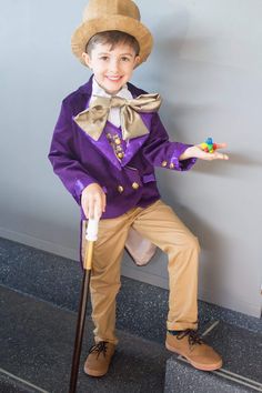 a young boy dressed up in a purple suit and hat with an old fashioned cane