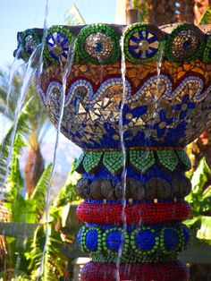 a large vase sitting on top of a lush green plant covered in lots of beads