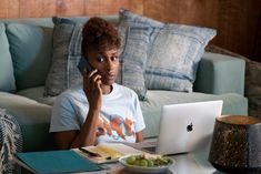 a woman sitting at a table in front of a laptop computer talking on the phone