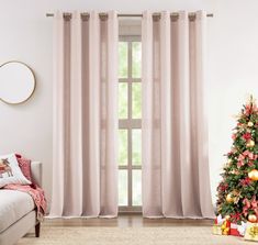 a living room with a christmas tree in the corner and pink curtains on the window