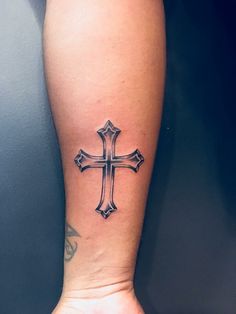 a cross tattoo on the left arm is shown in black and grey ink, with an arrow at the center