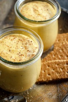 two small jars filled with food sitting on top of a wooden table next to crackers