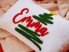 a white pillow with red and green embroidered words that says camp on it, sitting on a bed