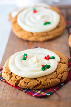 two cookies with white frosting and sprinkles sitting on a wooden board