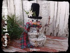 a crocheted snowman sitting on top of a wooden table next to plants