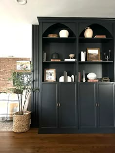 a black bookcase with shelves and vases on top of it in a living room