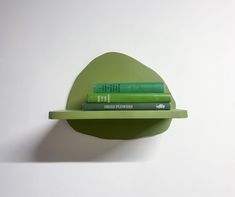 three books are sitting on a shelf with two green books in the middle and one is leaning up against the wall