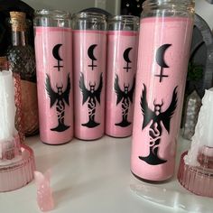 pink and black candles are sitting next to each other on the counter in front of bottles