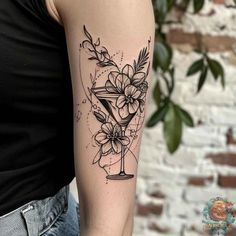 a woman with a tattoo on her arm holding a martini glass filled with flowers and leaves