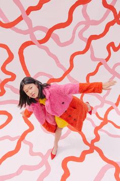 a woman in a pink coat and orange skirt standing on a white background with red wavy lines