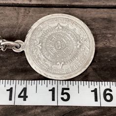 an antique silver pocket watch with a ruler next to it on a piece of wood