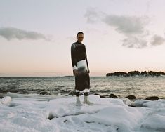 a man standing on top of snow covered ground next to the ocean with his surfboard