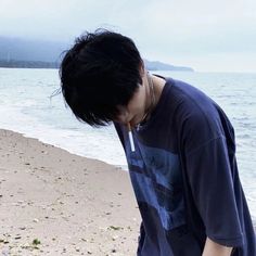 a young man standing on top of a sandy beach next to the ocean with his head in his hands