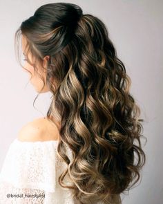 a woman with long curly hair in a half updo, wearing a white top