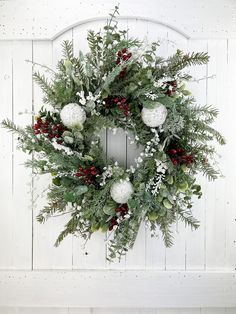 a christmas wreath hanging on the side of a white wooden wall with snowflakes and greenery