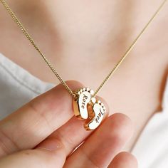 a woman is holding a gold necklace with two baby feet and the word love written on it