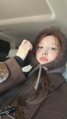 a woman with long hair wearing a brown jacket and scarf in the back seat of a car