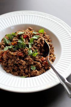 a white bowl filled with meat and garnished with cilantro on top