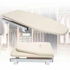 a white ironing board sitting on top of a metal rack with clothes hanging in the background