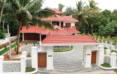 the house is surrounded by palm trees and white fenced in area with red tiled roof