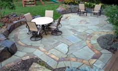 an outdoor patio with chairs and table in the middle of it, surrounded by landscaping