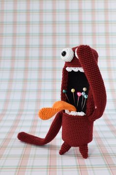 a crocheted red stuffed animal holding a carrot in it's mouth and eyes