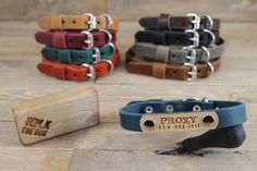 four different colored leather dog collars with engraved tags on them and one has a metal hook